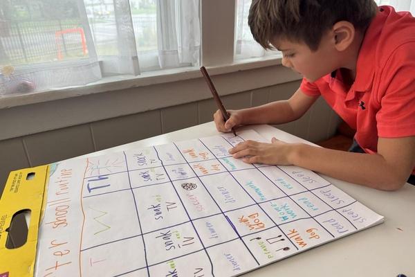 Child writing on a chart showing family routines.