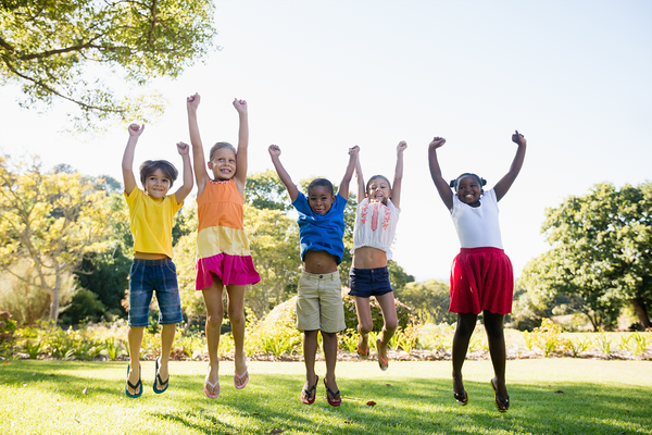 A row of children are jumping into the air at a local park.