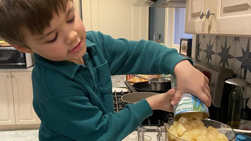 A child pours canned pineapple into a food processor.
