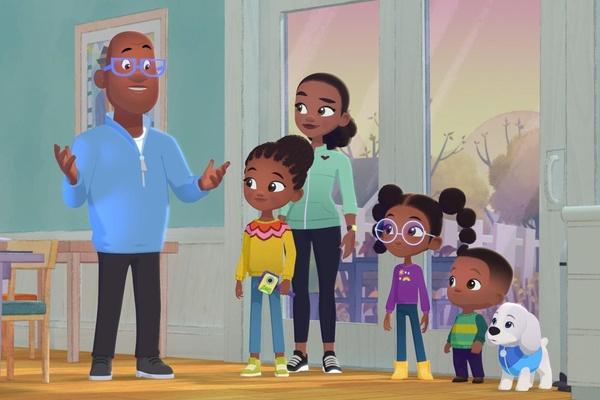 Al and his family are inside a house and standing together in front of a sliding glass door. A laptop is nearby and Al is explaining something to his family.