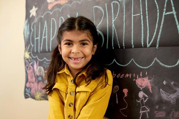 A child stand in front of a birthday party banner as it hangs on a wall.