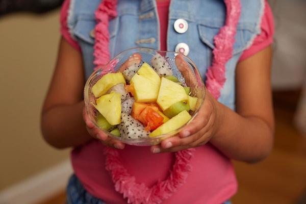 A child holds a cup of tropical fruit salad.