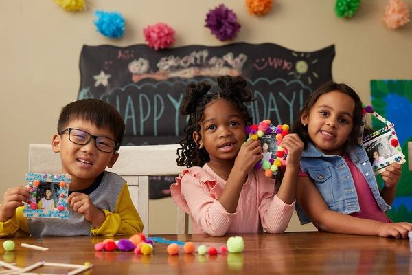 Three friends hold their popsicle stick picture frames.