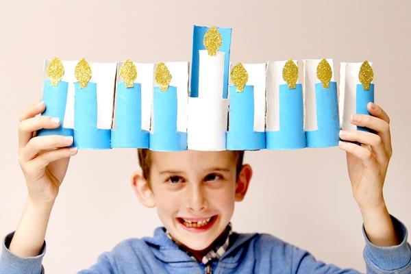 A child holds up their DIY Menorah Craft Using Cardboard.