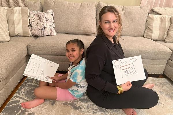 A parent and child hold up their drawings of the playground.