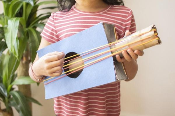 Girl holds a cardboard guitar.