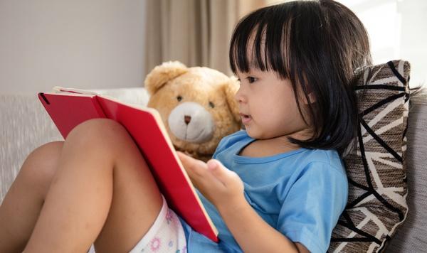 Preschool girl reading a book to her teddy bear.