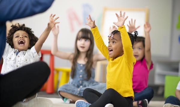 Group of children raising their hands in class.