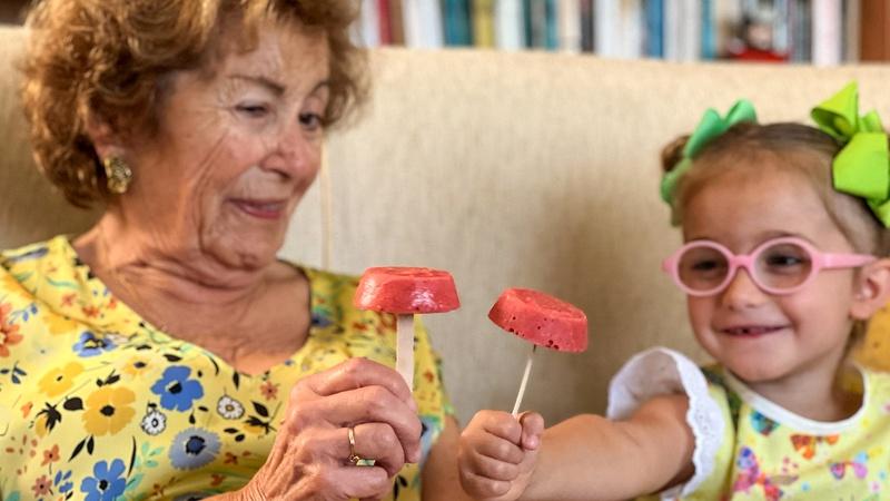 A child is enjoying a strawberry banana ice pop with her grandmother.