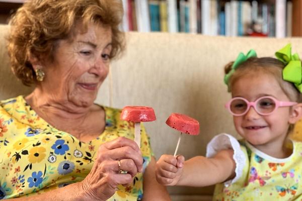 A child is enjoying a strawberry banana ice pop with her grandmother.