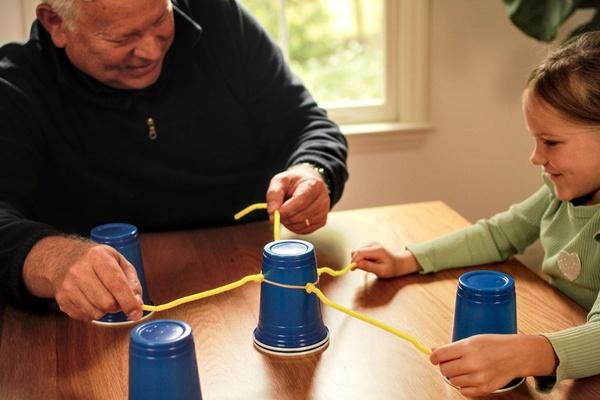 A grandfather and grandchild work as a team to stack cups.