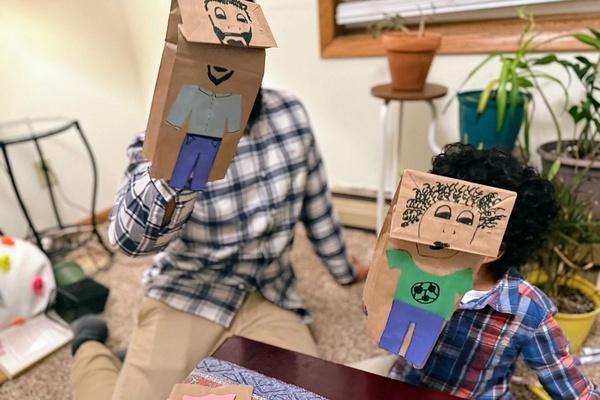 An adult and child show their completed paper bag puppets.