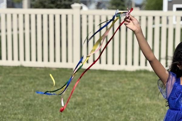 A child runs outside with a ribbon streamer blowing in the wind behind them.