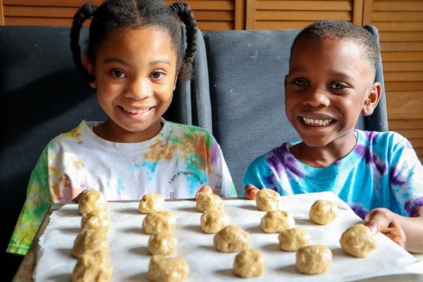 Dos niños sonríen frente a una bandeja para hornear con su masa de galletas “sácate el enojo” lista para meterla al horno.