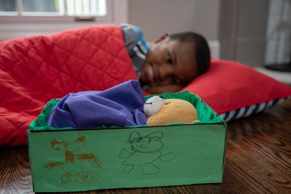 Un niño duerme junto a la camita que hizo para su peluche.