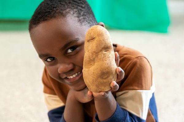 A boy smiles with a potato.