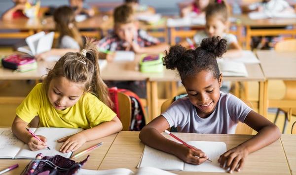 Two girls writing in their notebooks in class.