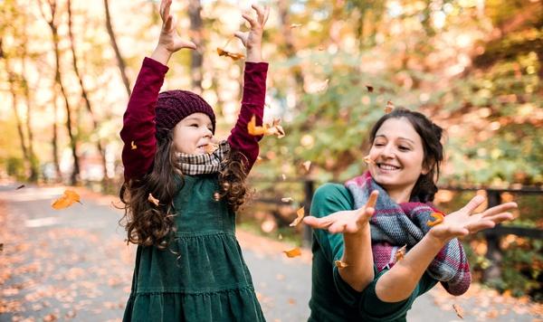 Mom and young daughter playing with autumn leaves.