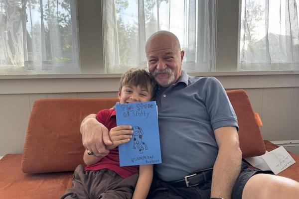 A child and his grandfather are sitting on a couch holding their finished storybook.