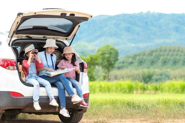 Parent and two children looking at a map while sitting in the tailgate of a car in a national park.