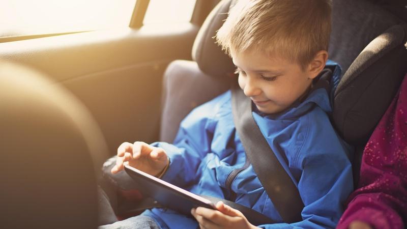 Child looking at a tablet while riding in a car.