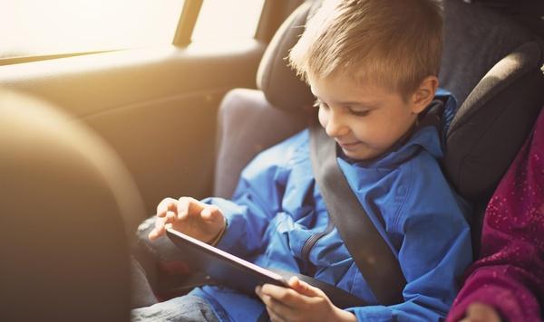 Young boy playing on a tablet in the car.