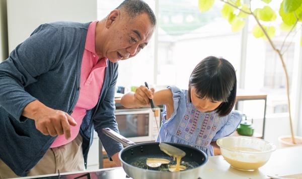 Grandfather and young granddaughter making pancakes together.