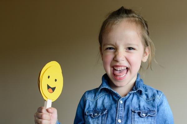 Girl smiling and holding popsicle stick with smiley face.