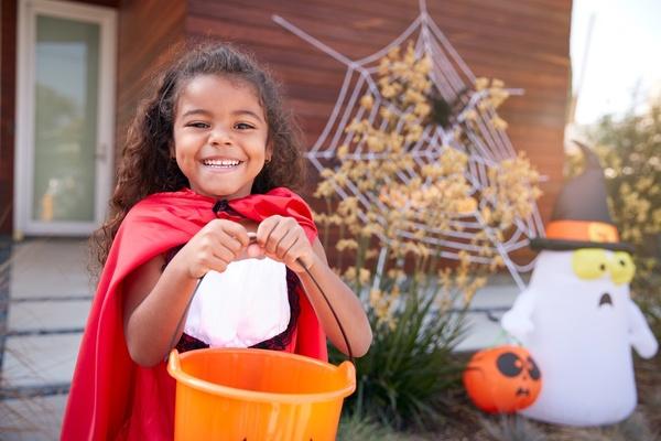 Girl wearing a cape and holding a Halloween bucket.