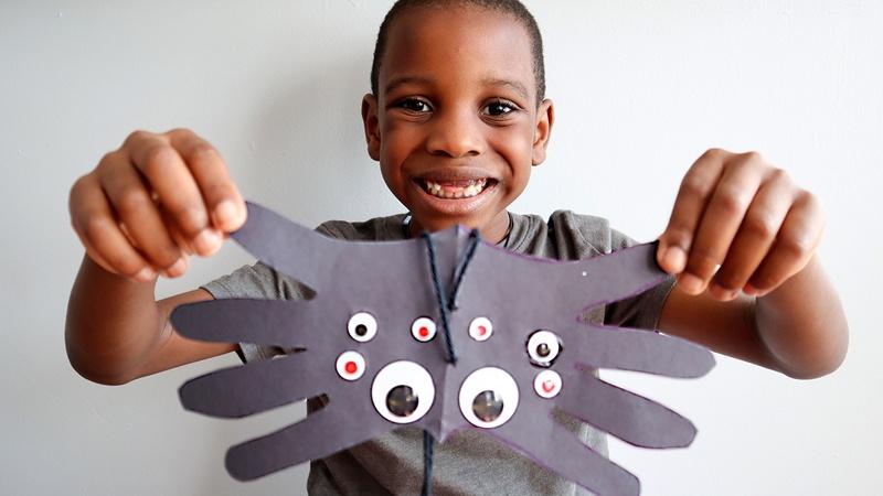 A child holding up his handprint spider craft.