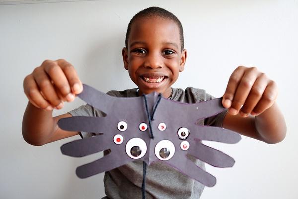A child holding up his handprint spider craft.