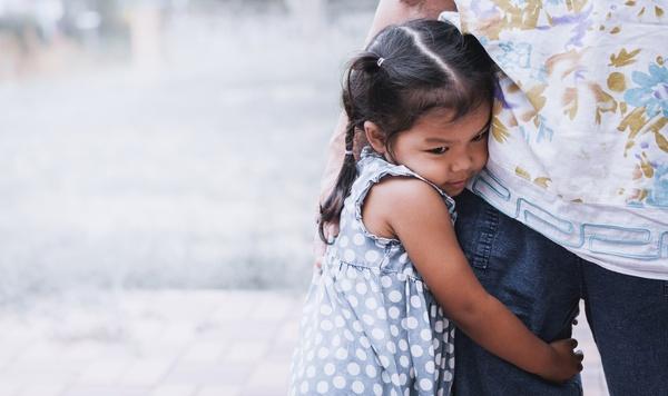 Image of little girl holding onto her father's leg.