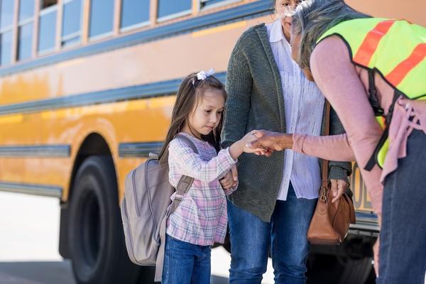A school bus driver shaking hands with a nervous child on the first day of school.