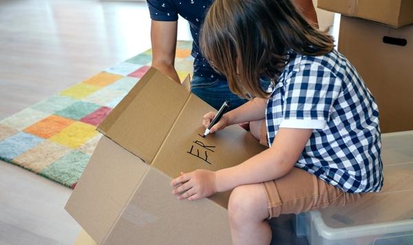 A child writing his name on a moving box.