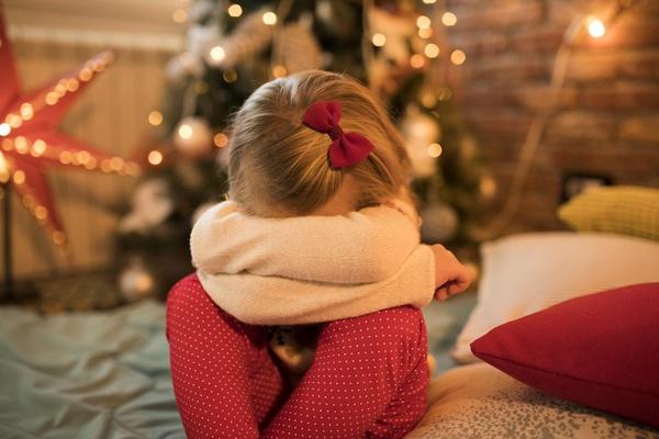 Young girl with her head in her arms in front of a Christmas tree.