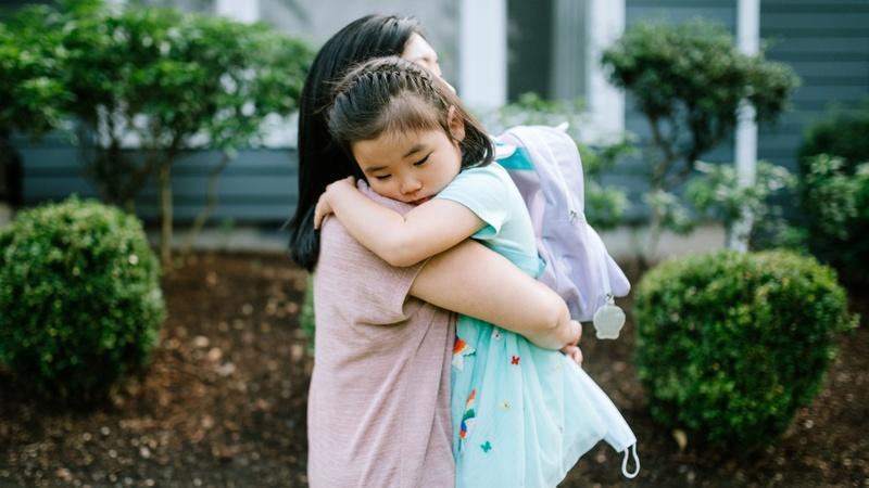 Una mamá abraza a su hija que lleva su mochila.