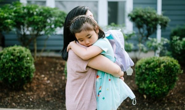Una mamá abraza a su hija que lleva su mochila.