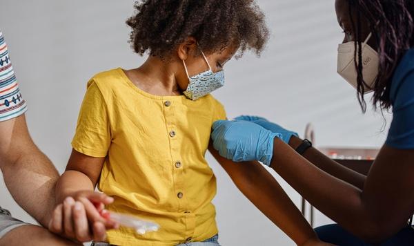 Young girl gets a shot from a doctor while holding her father's hand.