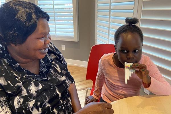 Image of child blowing into a homemade siku flute. An adult sitting with the child is smiling.