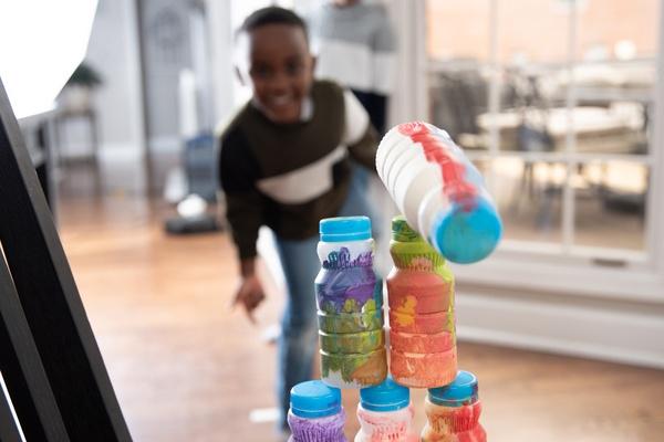 A child stands behind a stack of bottles. One bottle is toppling over.