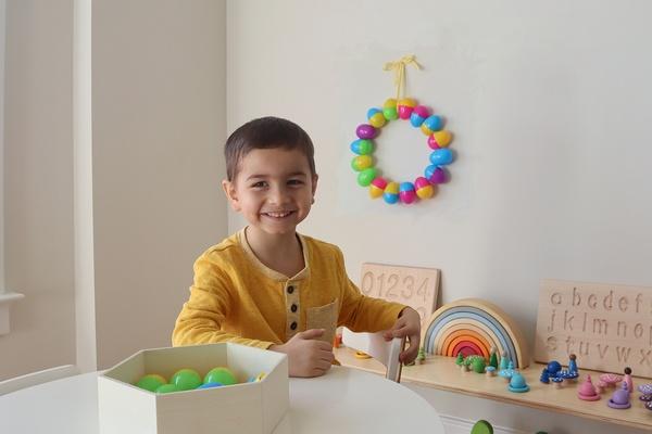 A finished Easter egg wreath hangs on a wall.