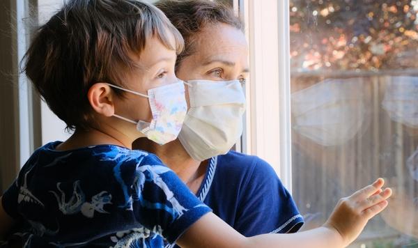 Mother and son wearing masks staring out the window.