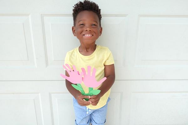 Young child holding handprint flowers craft.