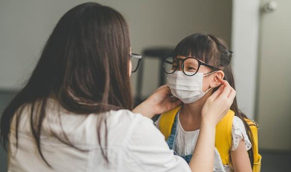 Mother helping her daughter put on a face mask.