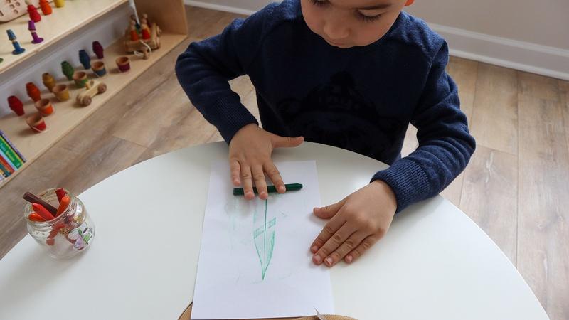 A child uses crayon and paper to make a leaf art project.