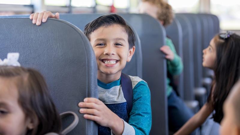 Schoolboy smiles excitedly while sitting in a school bus.