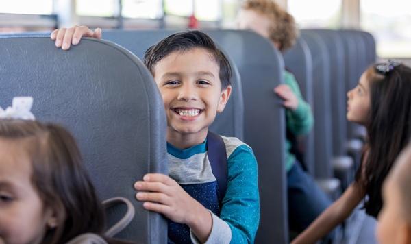 Schoolboy smiles excitedly while sitting in a school bus.