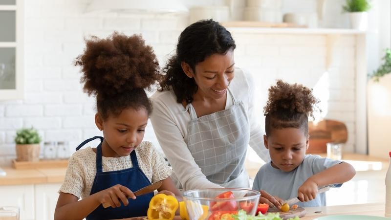 Two children helping their mom cut vegetables in the kitchen.