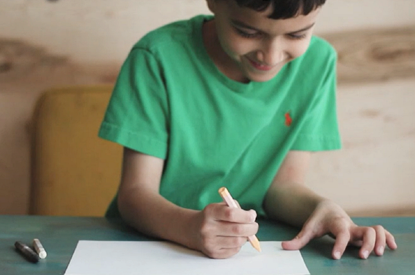 Imagen de un niño escribiendo en papel con un crayón de color claro.