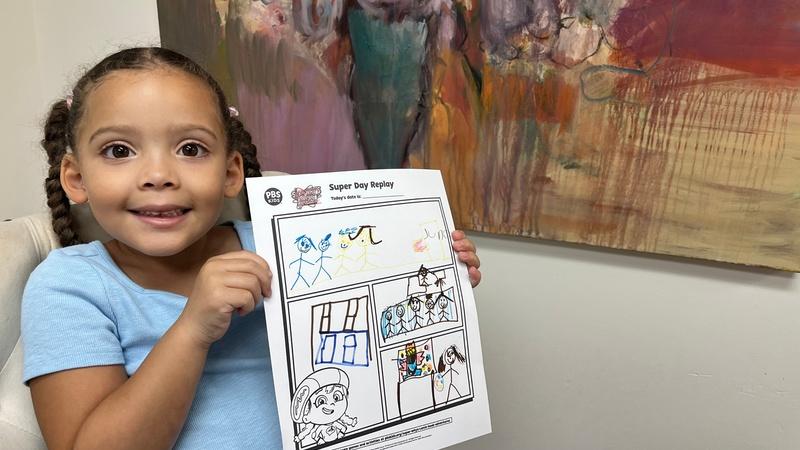 A child holds up her finished Super Day Replay printable showing her experience painting.